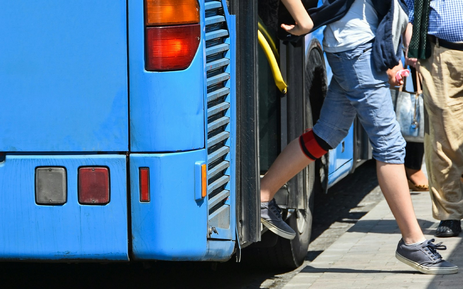 Person stepping off a blue tour bus onto a sidewalk.