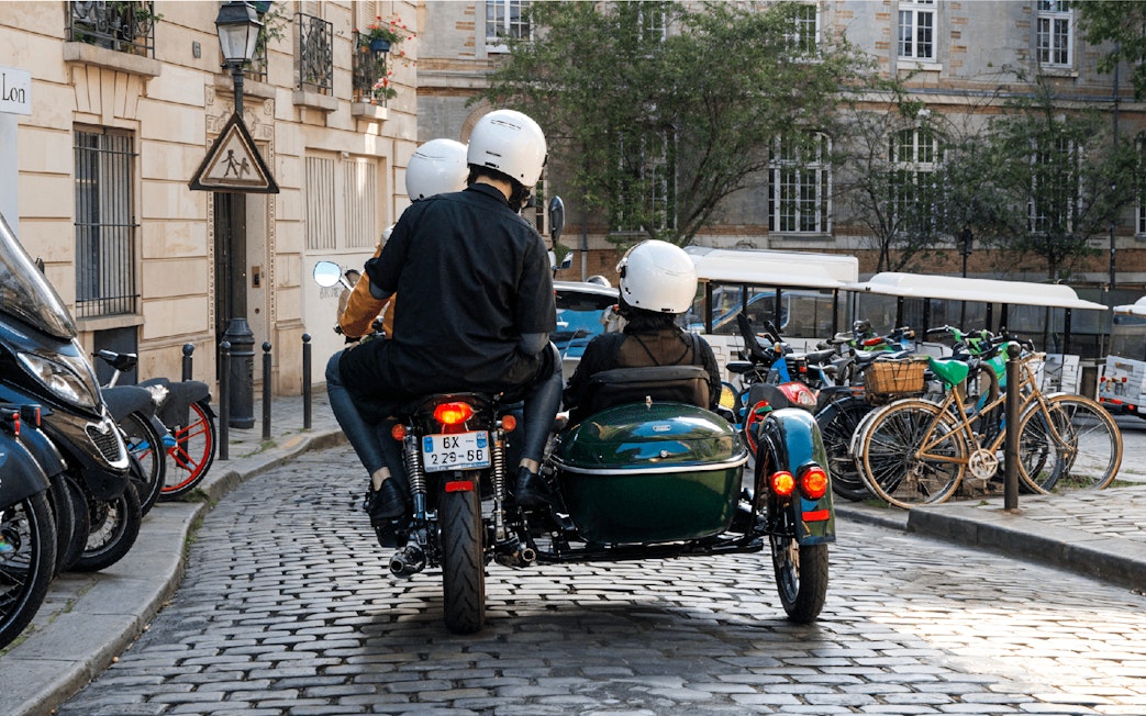 Sidecar tour on cobblestone street in Paris with riders wearing helmets.