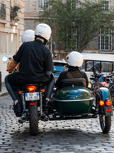 Sidecar tour on cobblestone street in Paris with riders wearing helmets.