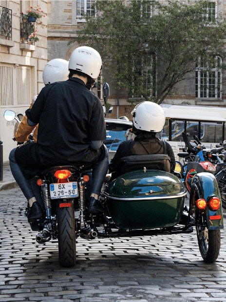 Sidecar tour on cobblestone street in Paris with riders wearing helmets.