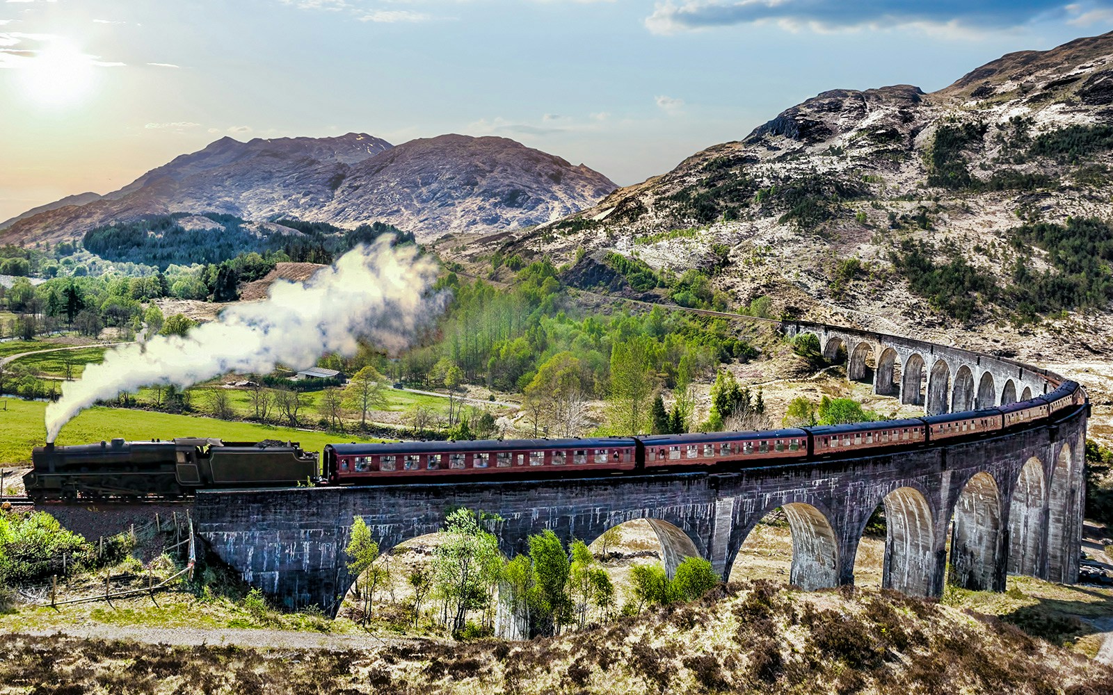 Steam train crossing Glenfinnan Viaduct on the West Highland Line, Scotland, with mountains in the background.