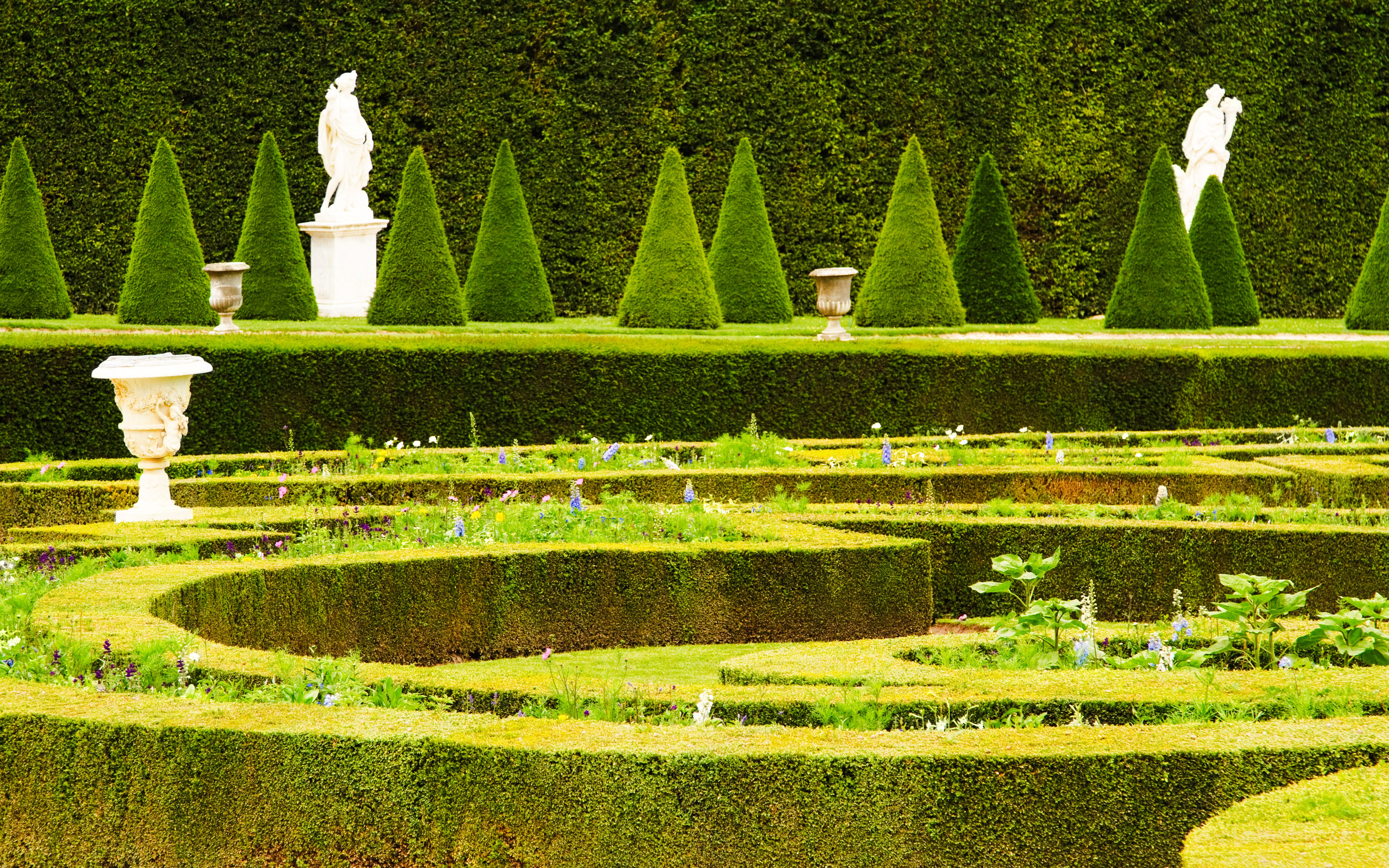 Versailles Gardens maze with manicured hedges, statues, and conical trees in France.