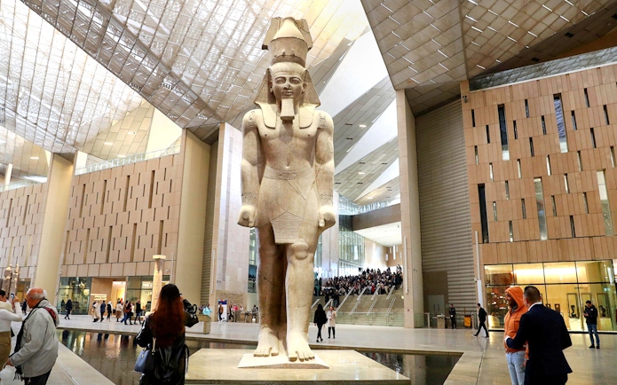 Grand Egyptian Museum interior with large pharaoh statue and visitors exploring.