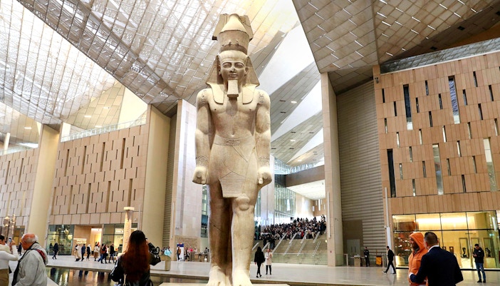 Grand Egyptian Museum interior with large pharaoh statue and visitors exploring.
