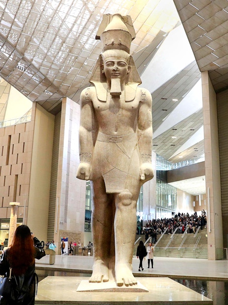 Grand Egyptian Museum interior with large pharaoh statue and visitors exploring.