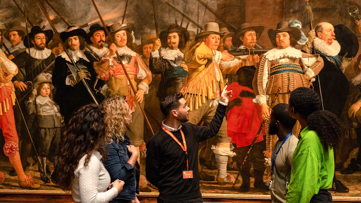 Tour guide explaining Rembrandt's "The Night Watch" to visitors at the Rijksmuseum.