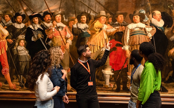 Tour guide explaining Rembrandt's "The Night Watch" to visitors at the Rijksmuseum.