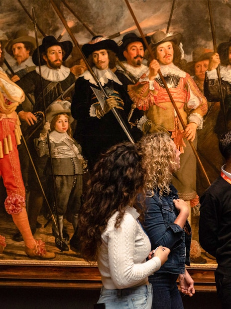 Tour guide explaining Rembrandt's "The Night Watch" to visitors at the Rijksmuseum.