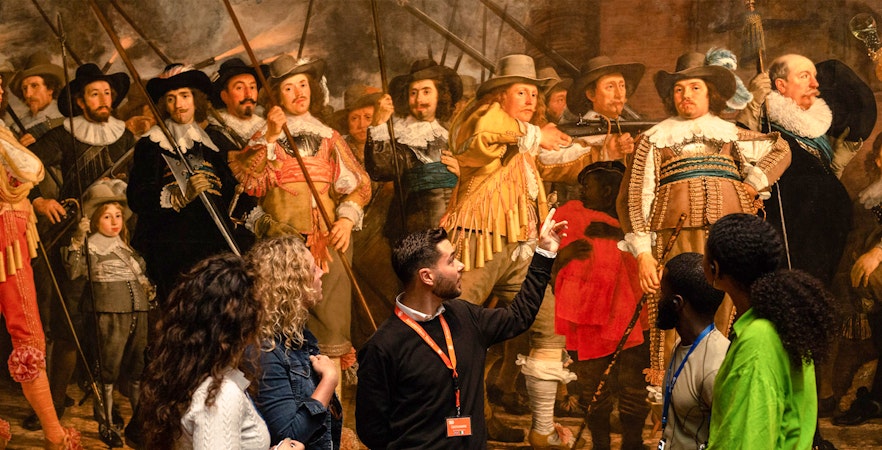 Tour guide explaining Rembrandt's "The Night Watch" to visitors at the Rijksmuseum.