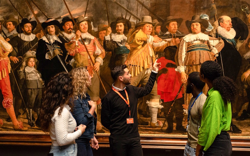 Tour guide explaining Rembrandt's "The Night Watch" to visitors at the Rijksmuseum.