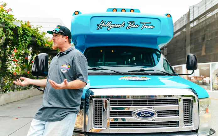 Guide speaking to tour group beside Hollywood Bus Tours vehicle, Los Angeles.