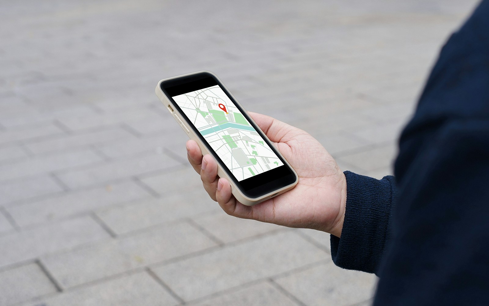 Mobile phone displaying map with location pin in user's hand.