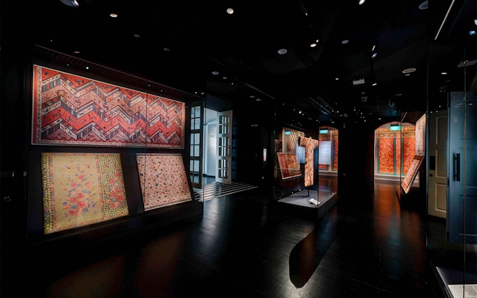 Dimly lit gallery with red and gold textiles at Peranakan Museum, Singapore.
