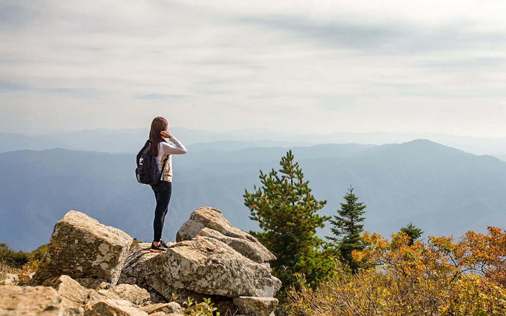 Female hiker on rocky peak in Seorak Mountain, South Korea, overlooking distant hills.
