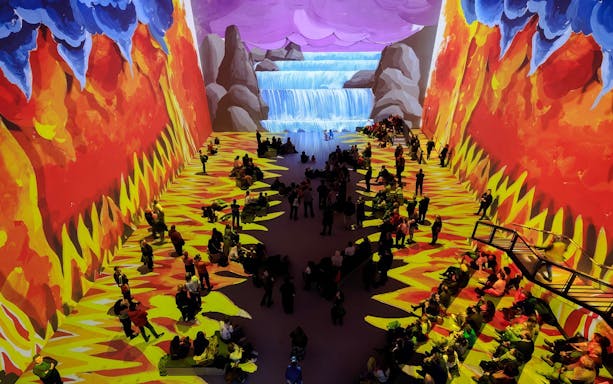 Visitors at David Hockney: Bigger & Closer exhibit, vibrant projections of nature scenes.