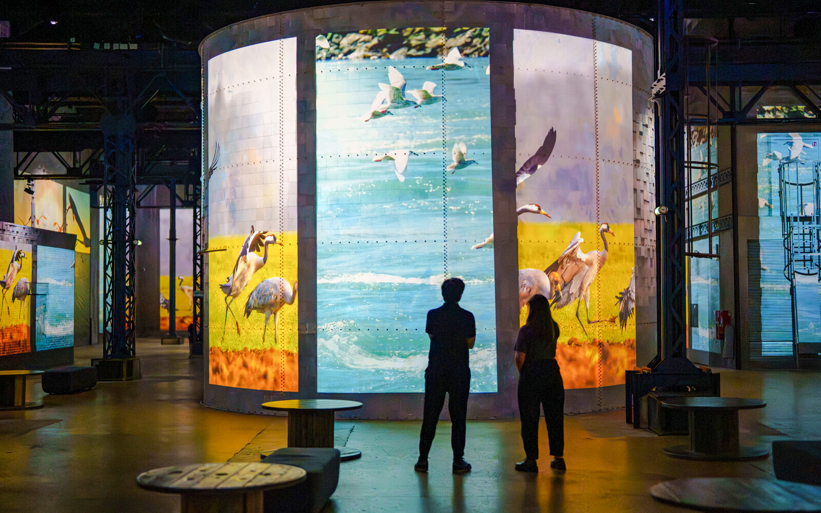 Visitors viewing dinosaur-themed digital art at Prehistoric Planet exhibition, Atelier des Lumières, Paris.