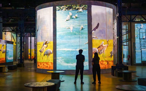 Visitors viewing dinosaur-themed digital art at Prehistoric Planet exhibition, Atelier des Lumières, Paris.