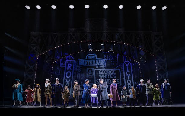 Stage performance of "Annie" with cast in period costumes under New Amsterdam Theatre lights.