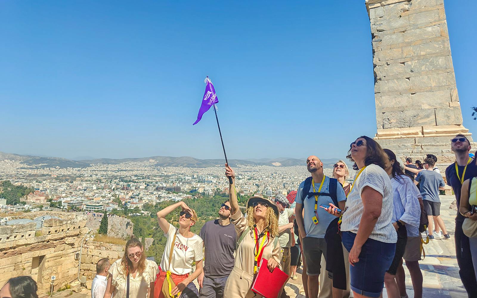 Tour group exploring the Acropolis in Athens with a guide holding a flag.