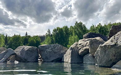 Rocky shoreline and lush trees at Chena Hot Springs, Alaska, under a cloudy sky.