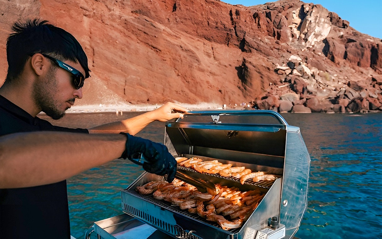Grilling seafood on a boat near Santorini's red cliffs.