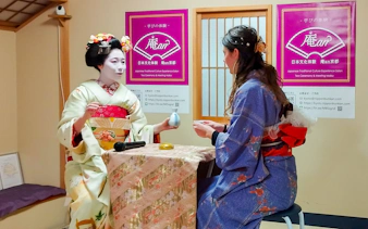 Maiko performing tea ceremony with a guest in traditional Japanese setting.