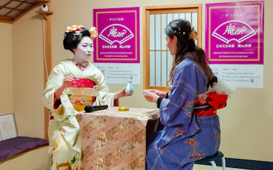 Maiko performing tea ceremony with a guest in traditional Japanese setting.