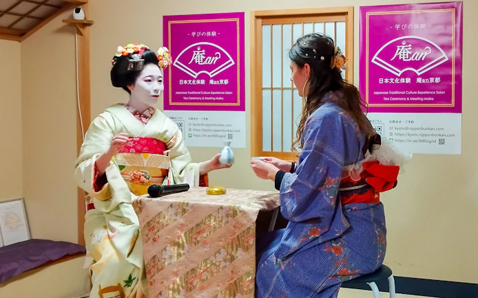 Maiko performing tea ceremony with a guest in traditional Japanese setting.
