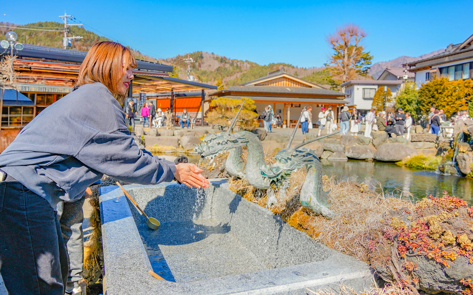 Tourist washing hands at dragon fountain in Oshino Hakkai, Japan.