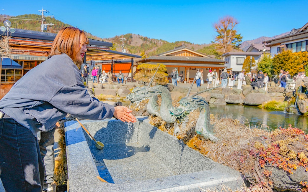 Tourist washing hands at dragon fountain in Oshino Hakkai, Japan.