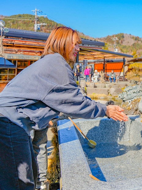 Tourist washing hands at dragon fountain in Oshino Hakkai, Japan.