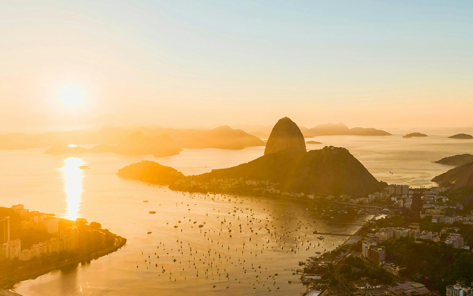 Aerial view of Rio de Janeiro at sunset with Sugarloaf Mountain in the background.