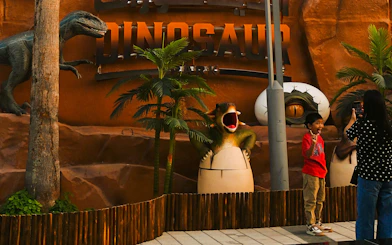 Child posing with dinosaur sculptures at Dubai Garden Glow's Dino Park.