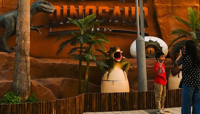 Child posing with dinosaur sculptures at Dubai Garden Glow's Dino Park.