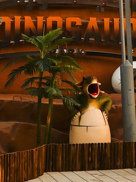 Child posing with dinosaur sculptures at Dubai Garden Glow's Dino Park.