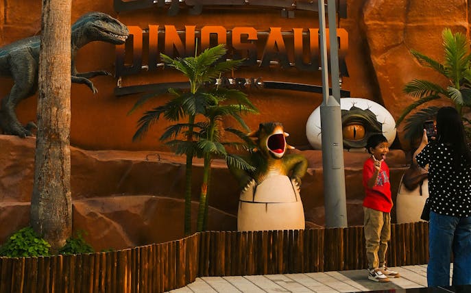 Child posing with dinosaur sculptures at Dubai Garden Glow's Dino Park.