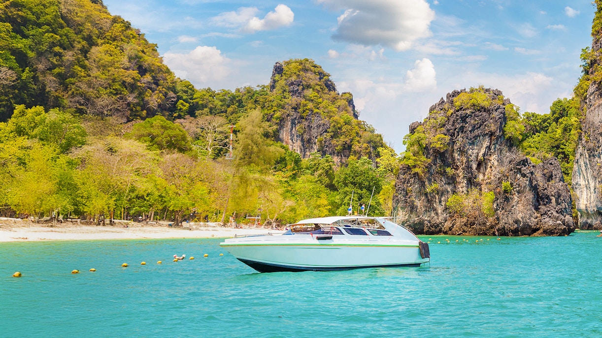 Speedboat on turquoise water near limestone cliffs, Hong Island, Thailand.