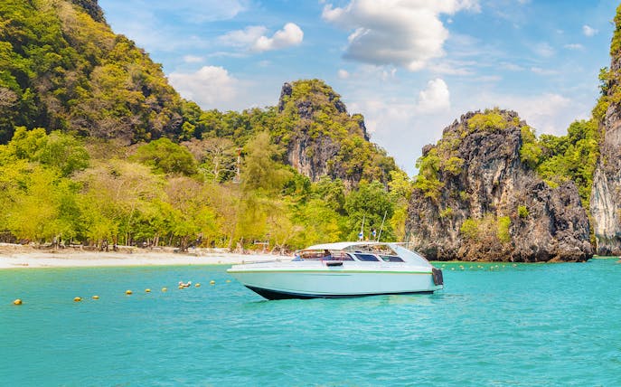 Speedboat on turquoise water near limestone cliffs, Hong Island, Thailand.