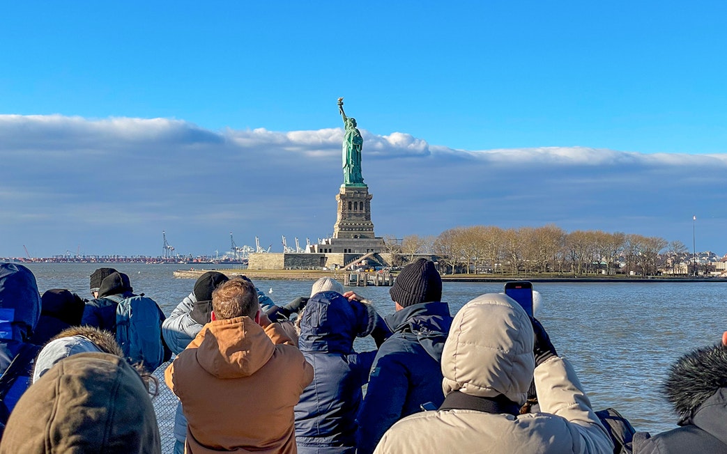Tourists photographing the Statue of Liberty from a sightseeing cruise in New York Harbor.