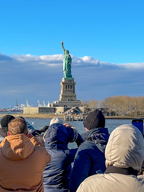 Tourists photographing the Statue of Liberty from a sightseeing cruise in New York Harbor.