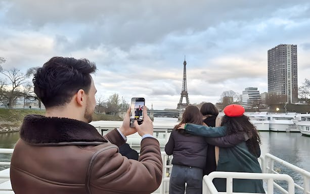 Tourists on Seine River cruise photographing Eiffel Tower, Paris.