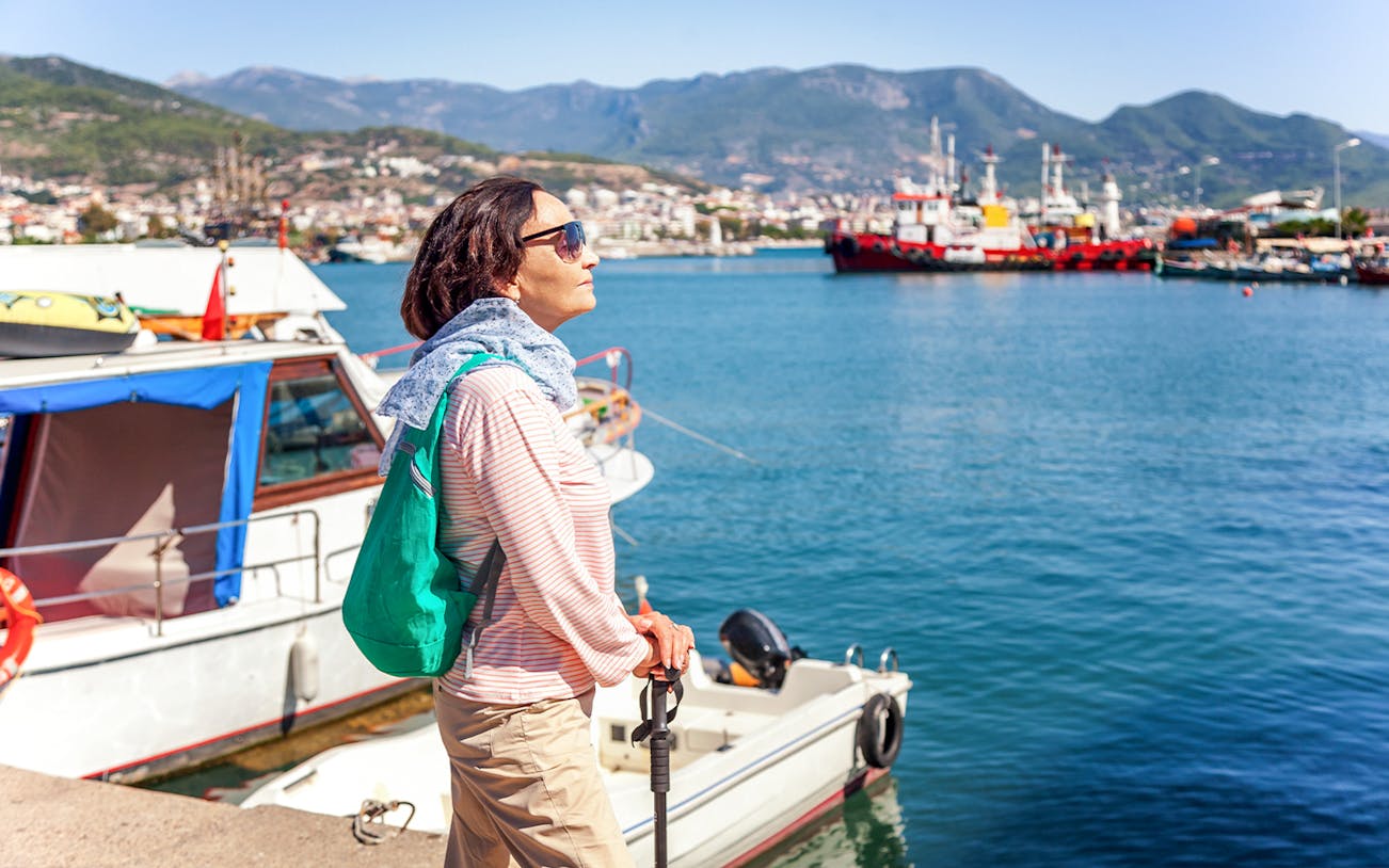 Person enjoying the view at Alanya harbor with boats and mountains in the background.