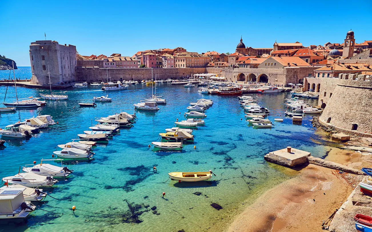 Boats in Dubrovnik's medieval harbor with historic city walls in the background.