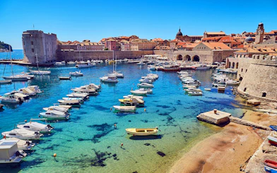 Boats in Dubrovnik's medieval harbor with historic city walls in the background.