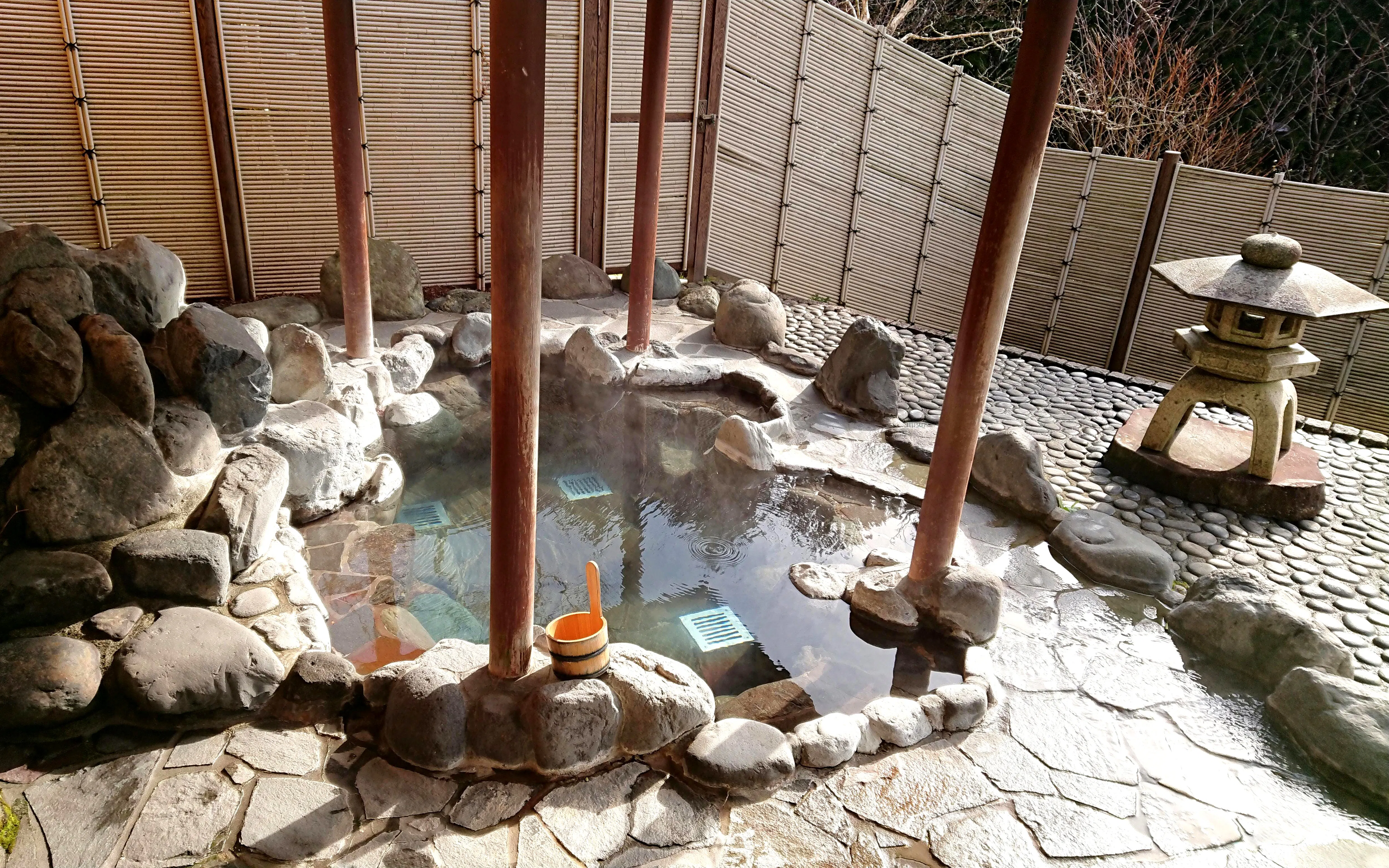 Outdoor onsen hot spring in Hakone, Japan, with stone surroundings and a traditional lantern.