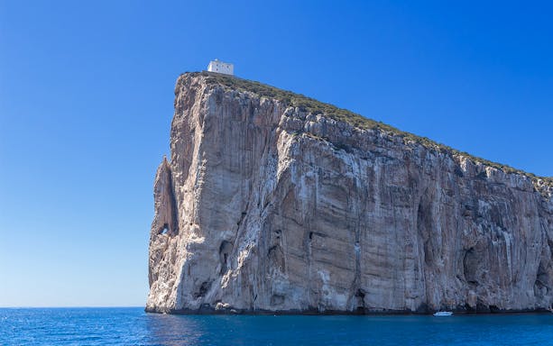 Cliffside view of Alghero Bay with a boat on the water, seen during a tour from Fertilia.