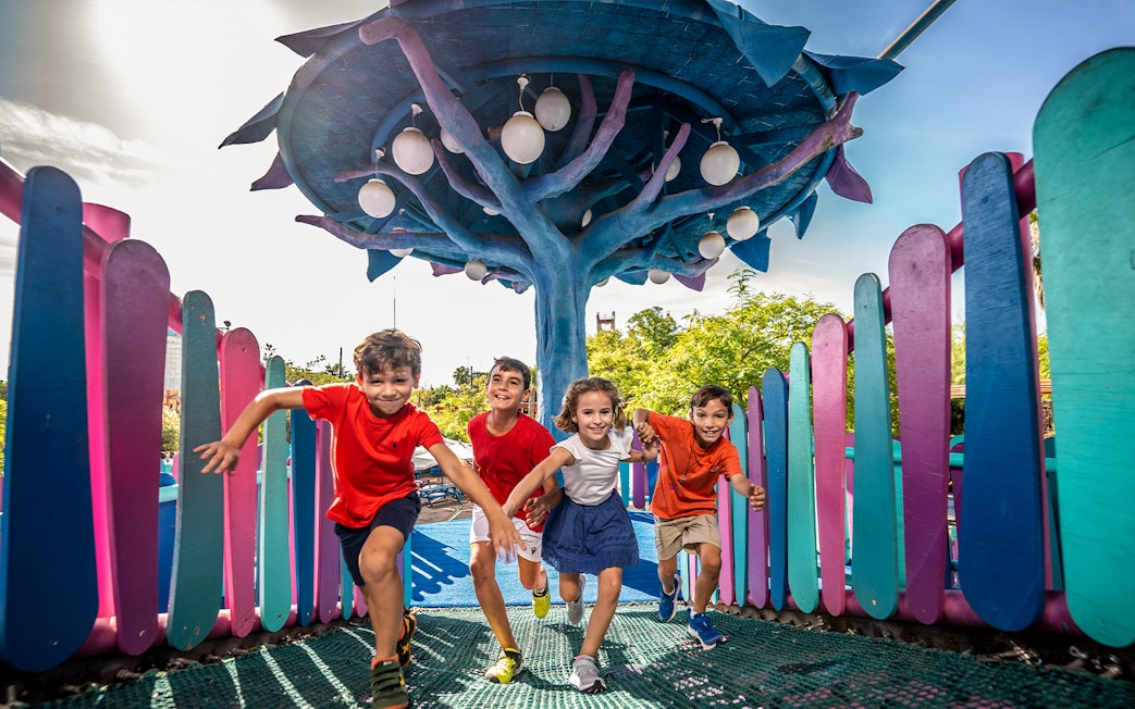 Children playing at Isla Mágica adventure area under a colorful tree structure.