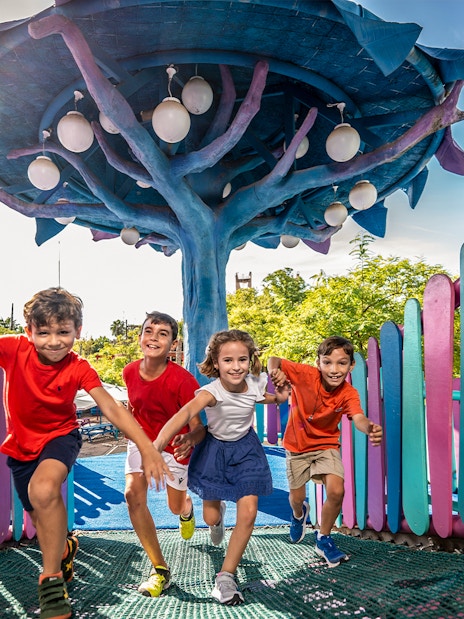 Children playing at Isla Mágica adventure area under a colorful tree structure.