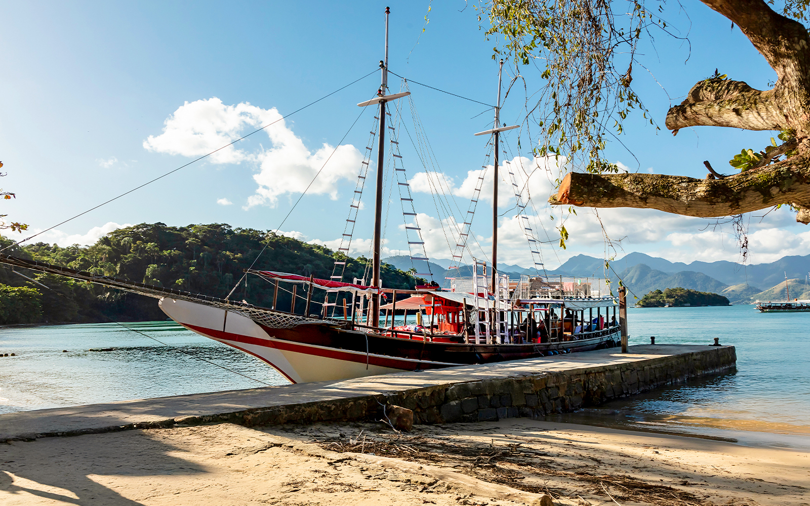 Tourist catamaran docked at pier on Ilha Grande with lush hills in background.