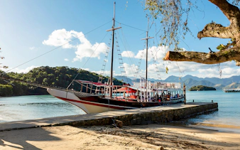 Tourist catamaran docked at pier on Ilha Grande with lush hills in background.